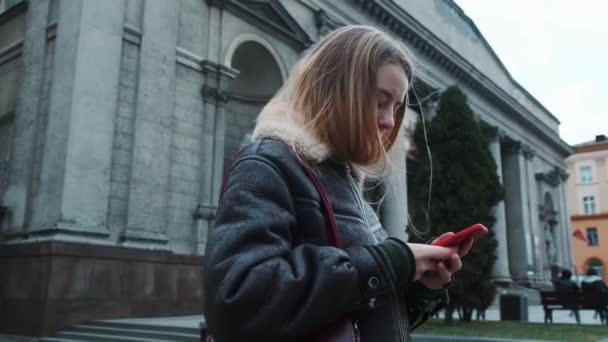 Portré egy lányról, aki a szabadban gépel egy mobiltelefonon. Közelkép egy lányról, akinek telefon van a kezében, városi háttérrel.. — Stock videók