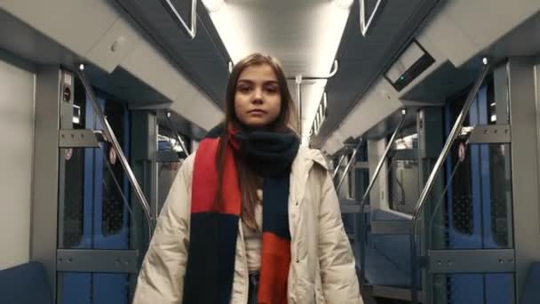 Uma rapariga com um cachecol brilhante anda de metro. Um carro de metrô vazio e uma garota olhando para a moldura. — Vídeo de Stock