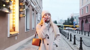 Şapkalı ve atkılı güzel bir kız şehir merkezinde yürüyor ve telefonda konuşuyor. Kız ışıklarla süslenmiş şehre hayran.. 