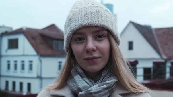 Κοντινό πλάνο μιας νεαρής Ευρωπαίας με λευκό καπέλο που κοιτάζει στην κάμερα στο βάθος της πόλης. Πλάνα αργής κίνησης της πόρτερ.. — Αρχείο Βίντεο