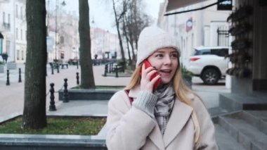 Şapkalı ve atkılı güzel bir kız şehir merkezinde yürüyor ve telefonda konuşuyor. Kız ışıklarla süslenmiş şehre hayran.. 