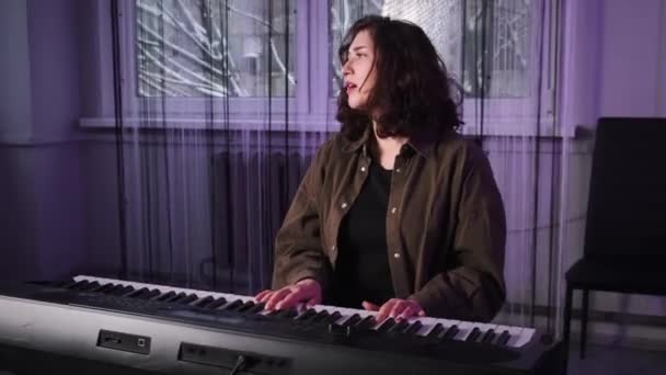 Une fille aux cheveux bouclés joue du piano et chante. Une fille d'apparence orientale joue du piano. Cours de chant. — Video