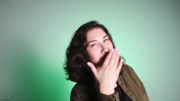 Een meisje tegen een witte muur met een felle groene achtergrondverlichting toont een emotie van verrassing. Portret van een jong meisje van blanke verschijning. — Stockvideo