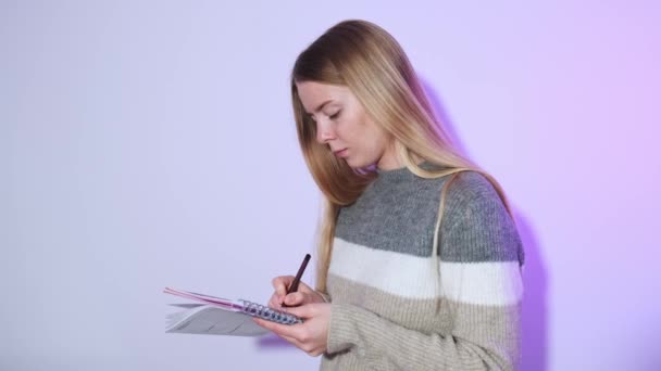 Close-up de uma bela jovem estudante loira, segurando cadernos e, olhando para a câmera e sorrindo para o cenário brilhante com iluminação de fundo. — Vídeo de Stock