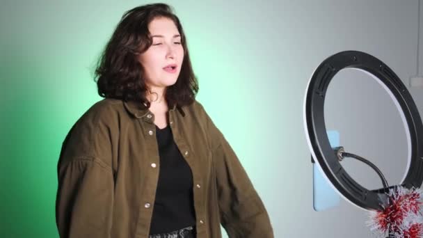 Vertikales Video. Ein Mädchen mit dunklem lockigem Haar tanzt für die Kamera gegen eine Wand. Nimmt ein Video für soziale Medien auf. — Stockvideo