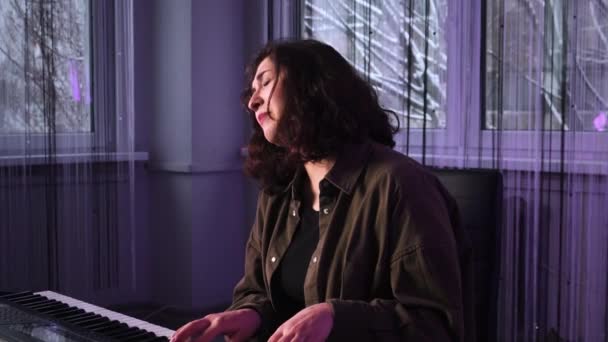 Ένα νεαρό κορίτσι με σκούρα μαλλιά απολαμβάνει να παίζει πιάνο. Ένα κορίτσι στο στούντιο παίζει πιάνο.. — Αρχείο Βίντεο