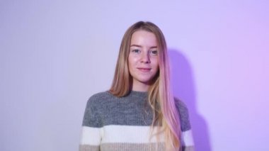 Sarışın bir kızın parlak bir arkaplanda parmaklarını kaldırıp gülümsediği bir fotoğraf. Parlak ve ışıl ışıl duygular.