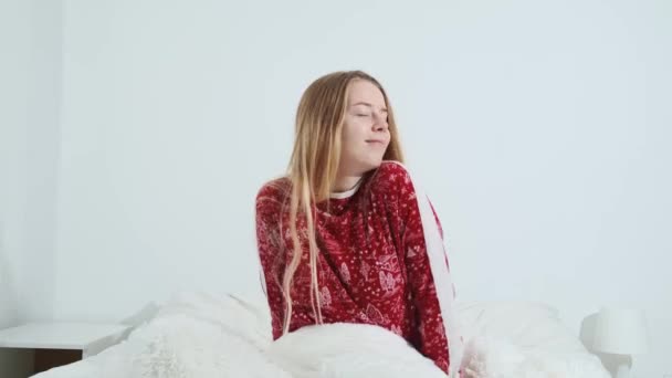 A calm young girl wakes up in a comfortable, cozy, fresh bed in red pajamas, enjoying a healthy, strong day. — Stockvideo