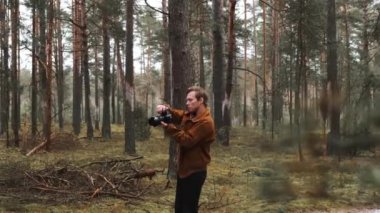 Genç sarışın bir erkek fotoğrafçı doğanın fotoğraflarını çekiyor. Fotoğrafçı, kış çiftiyle ormanda fotoğraf çekiyor. Genç fotoğrafçı. 
