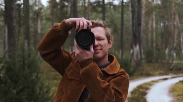 Un giovane fotografo maschio biondo fotografa la natura. Fotografo scatta foto nel bosco nella coppia invernale. Giovane fotografo. — Video Stock