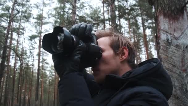 Um jovem fotógrafo loiro tira fotos da natureza. Fotógrafo tira fotos na floresta no casal de inverno. Jovem fotógrafo. — Vídeo de Stock