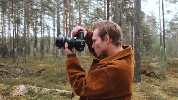 Un giovane fotografo maschio biondo fotografa la natura. Fotografo scatta foto nel bosco nella coppia invernale. Giovane fotografo. — Video Stock