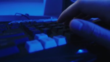 Oyun oynamak ve parlak mavi arkaplan üzerinde çalışmak için klavye kullanan bir oyuncunun yakın plan görüntüsü.