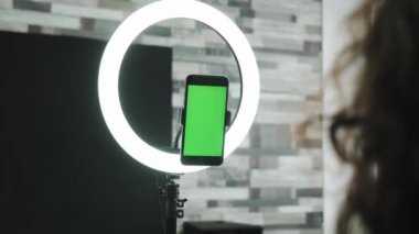 Üç ayaklı yeşil ekranlı telefon ve yüzük lambası. Öğretmen öğrencileriyle konuşuyor ya da çalışıyor.. 