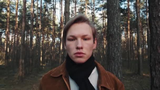 Um jovem loiro de pé no fundo da floresta. Close-up de um jovem com um rosto sério. — Vídeo de Stock