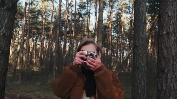 Genç sarışın bir erkek fotoğrafçı doğanın fotoğraflarını çekiyor. Fotoğrafçı ormanda eski bir kamerayla fotoğraf çekiyor. Eski tarz giyinmiş genç fotoğrafçı.. — Stok video
