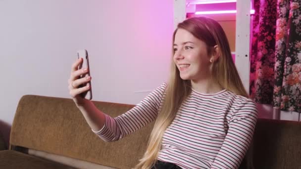 Primer plano de una joven hablando en una videollamada con su teléfono sentado en el sofá. — Vídeos de Stock