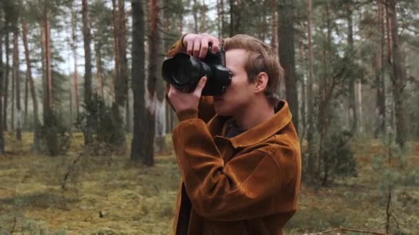 Um jovem fotógrafo loiro tira fotos na floresta. Fotógrafo na natureza. — Vídeo de Stock
