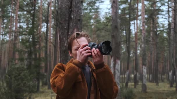 Un joven fotógrafo rubio toma fotos en el bosque. Fotógrafo en la naturaleza. — Vídeo de stock
