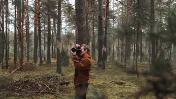 Ένας φωτογράφος βγάζει φωτογραφίες στο δάσος, ένας νεαρός βγάζει φωτογραφίες στο δάσος με την κάμερα του. Όμορφη φύση μέσα από τα μάτια ενός φωτογράφου. — Αρχείο Βίντεο