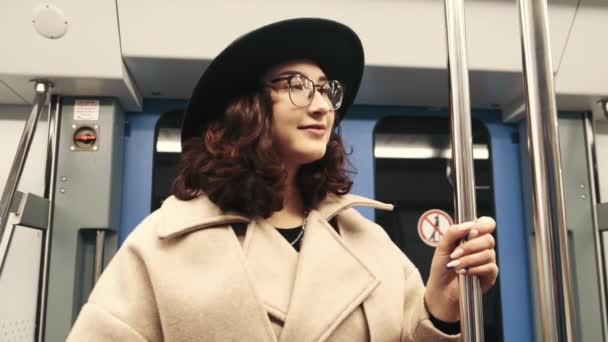 Ein Mädchen mit lockigem Haar und Hut fährt in der U-Bahn und hält sich am Geländer fest. Ein Mädchen fährt in der U-Bahn. — Stockvideo