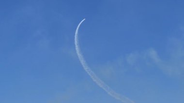 Airplane draws a large circle in the blue sky with its white smoke