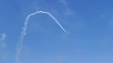 Aerobatic airplane does an half cuban eight with white trail in blue sky