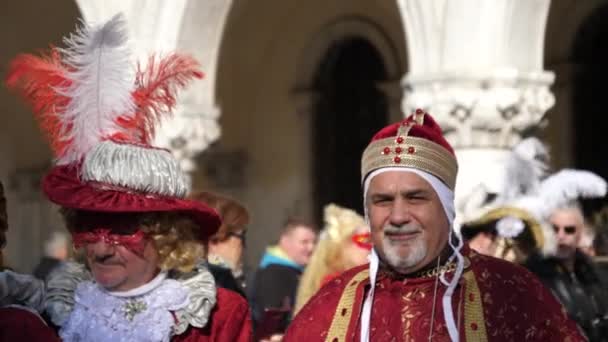 Två personer talar varandra med karneval drees, turister i bakgrunden — Stockvideo