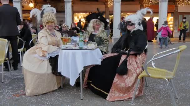 Ženy s karnevalovými kostýmy a maskami sedící u stolu během karnevalu — Stock video