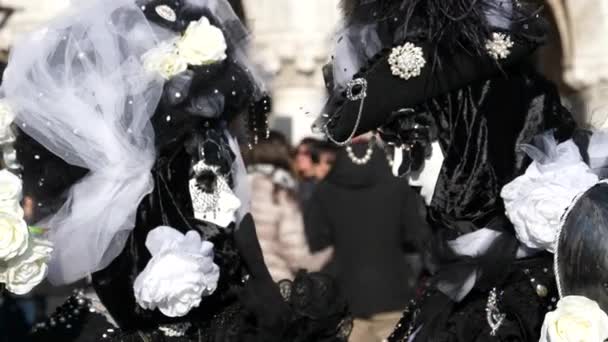 Een echtpaar gekleed in zwart-wit kostuums met Venetiaanse maskers met stok — Stockvideo