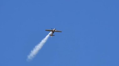 Sarı akrobatik uçak açık mavi gökyüzünde ustalık gerektiren akrobatik manevralar yapıyor.