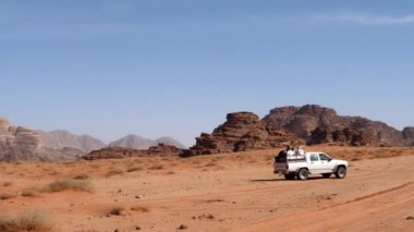 4x4 off-road aracı, çöldeki kırmızı kumda turistlerle birlikte çalışıyor.
