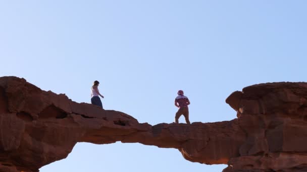 Coppia di turisti uomini e donne che camminano su un ponte di roccia naturale. Cielo blu sfondo — Video Stock