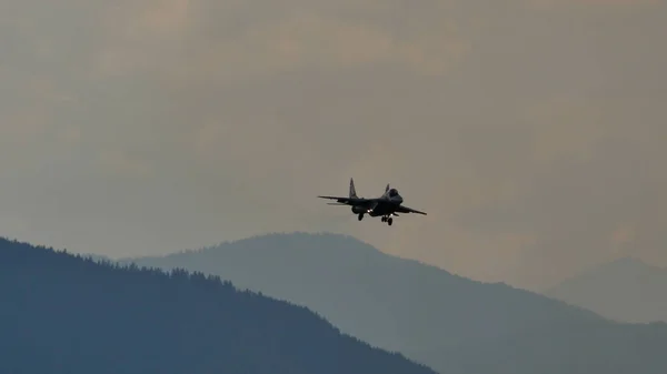 青の山を背景に軍用ジェット機着陸の小さなシルエット — ストック写真