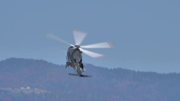 Helikopter lågt flyger i blå himmel med grön skog på berg i bakgrunden — Stockvideo