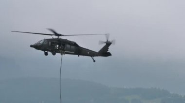 Uçan bir askeri helikopter, askerlerin indiği bir halat fırlatıyor.