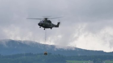 Helikopter havada iple asılı halde askeri malzeme taşıyor.