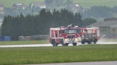 Zeltweg, Avusturya SEPTEMBER, 6, 2019 Havalimanı itfaiye kamyonları çok kötü hava koşullarında düşen bir uçağı kurtarmak için acele ediyorlar. İsveç Hava Kuvvetleri 'nin FVM CVM O1 Tummelisa rotary Le Rhone motoru