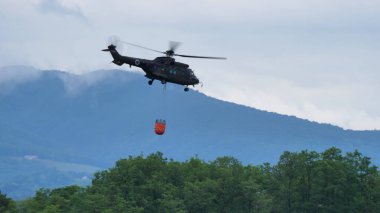 Cerklje Slovenya Mayıs 29, 2022 Yangın helikopteri ateşe atmak için bir kova dolusu suyla bir ormanın üzerinde uçuyor. Slovenya Hava Kuvvetleri 'nden Eurocopter AS532 Cougar Airbus Helikopterleri. Boşluğu kopyala