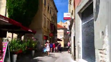 Pula Croatia AUGUST, 15, 2020 Hyperlapse in 4K walking on central historical road and ending at town hall square full of tourists eating on restaurant dehors. Temple of Augustus. Croatia flags