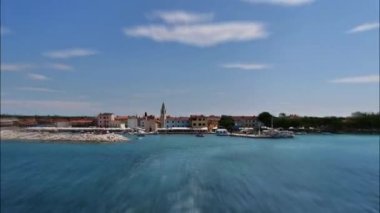 Arka planda Fazana balıkçı köyü ve ön planda Hırvat bayrağı bulunan Hırvat Ulusal Parkı Brijuni Adaları 'na giden bir feribot gemisinden hiperlapa..