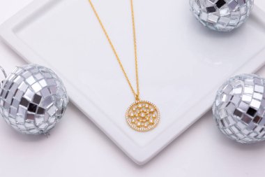 Beyaz bir arka planda, beyaz bir tabakta altın bir kolye ve etrafında disko topları..