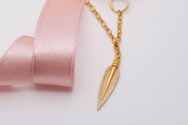 Pembe kurdeleli, altın kaplamalı kadın kolyesi. Yumuşak beyaz arka planda..