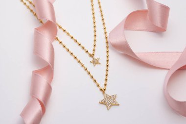 Yumuşak beyaz arka planda pembe kurdeleli elmas kaplama altın kolyeler..