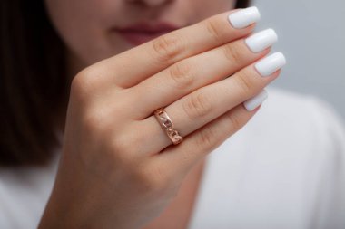 Beyaz bir elbise içinde beyaz ojeli genç bir kadın manken katlanmış gümüş bir yüzükle poz veriyor.