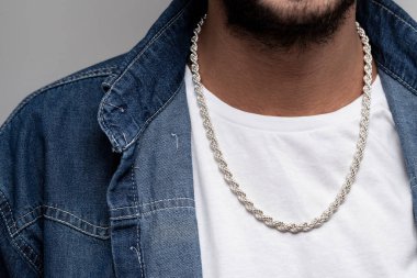 Beyaz tişörtlü ve mavi kot gömlekli genç erkek model gümüş zincirli poz veriyor..