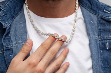 Beyaz tişörtlü ve mavi kot gömlekli genç erkek model gümüş zincirli poz veriyor..