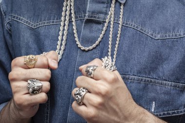 Beyaz tişört ve mavi kot gömlekli genç erkek model gümüş yüzük ve gümüş zincirli poz veriyor..