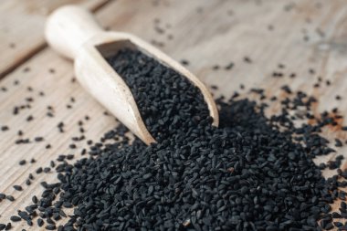 Siyah kimyon tohumları ve ahşap kepçe, doku arka planı.