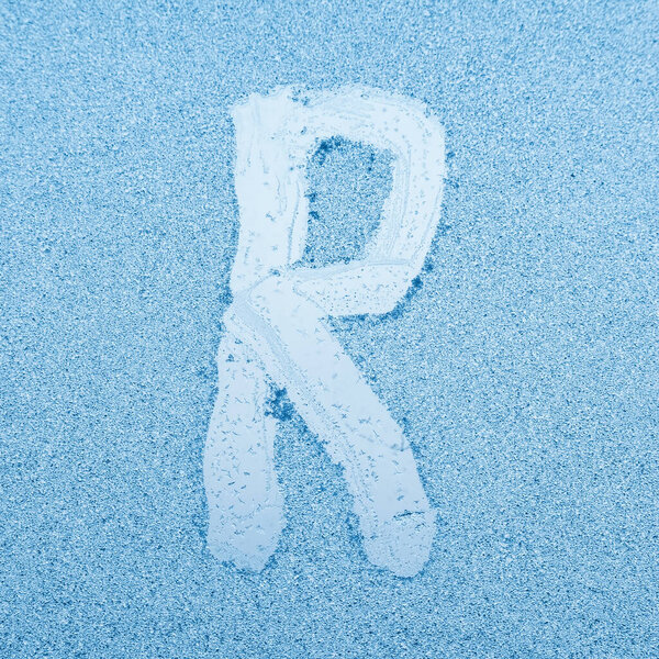 The letter R written on glass with frost in the frost in winter, close up.